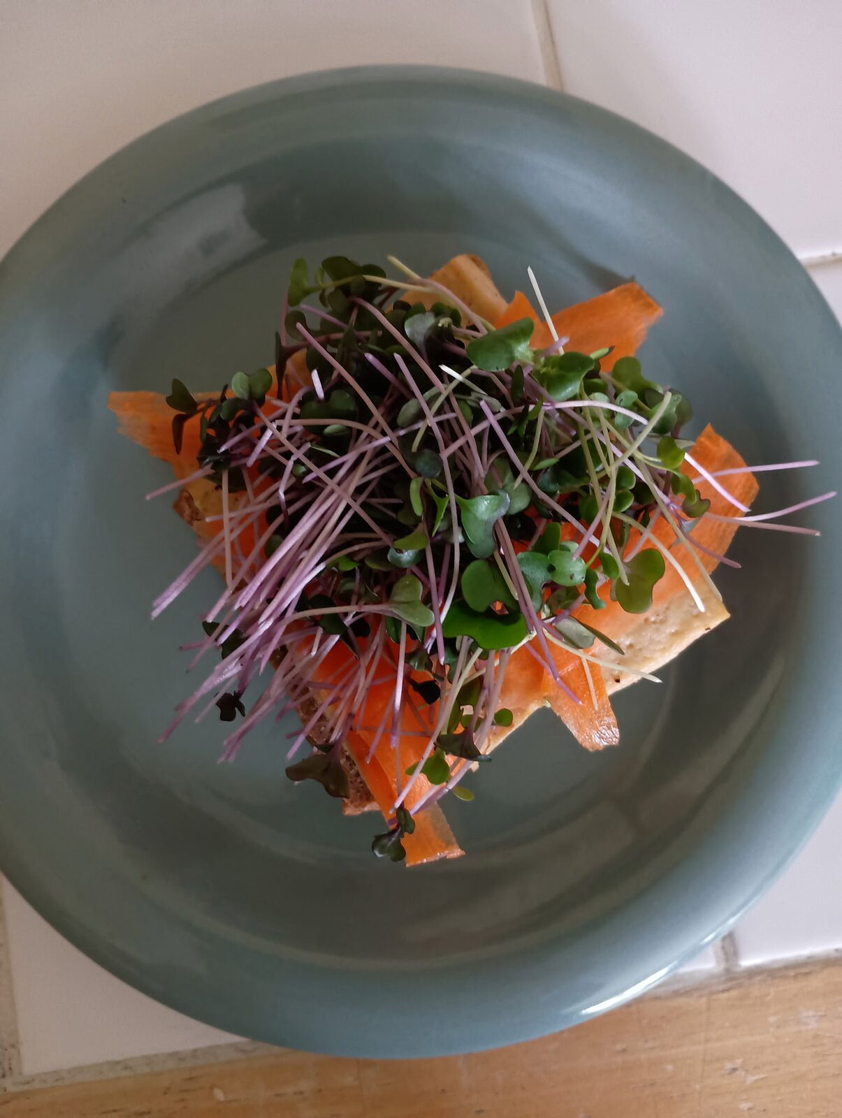 A green ceramic plate piled with crackers, orange cheese, and a generous tangle of pink-stemmed microgreens.